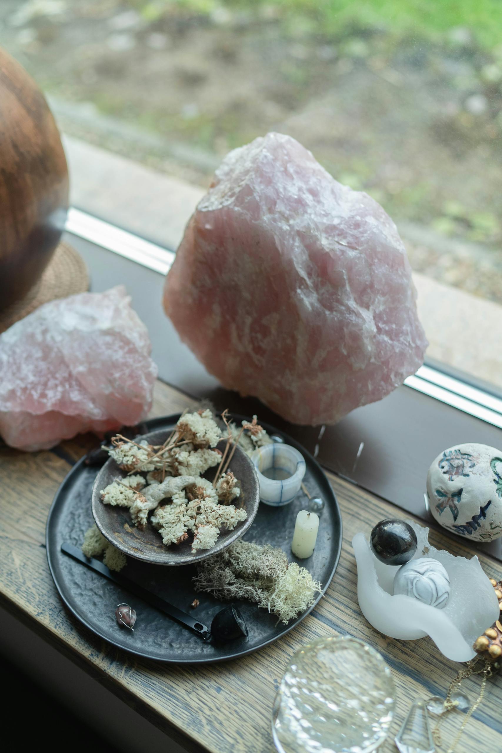 A creative display of crystals, dried herbs, and spiritual items on a wooden table by the window.
