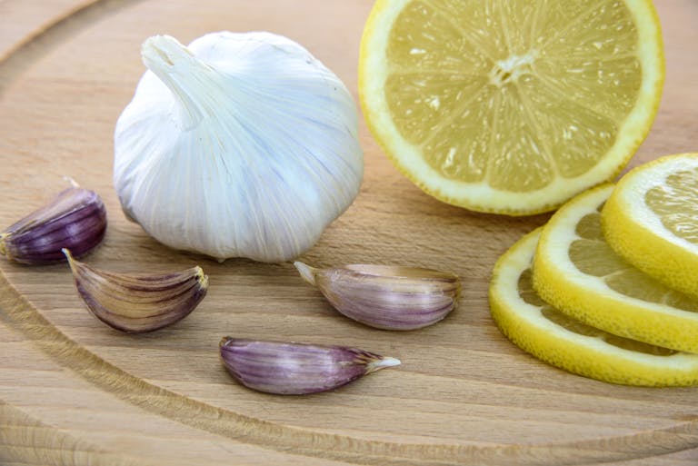 Close-up of fresh garlic and lemon slices on a wooden board, ideal for healthy cooking.